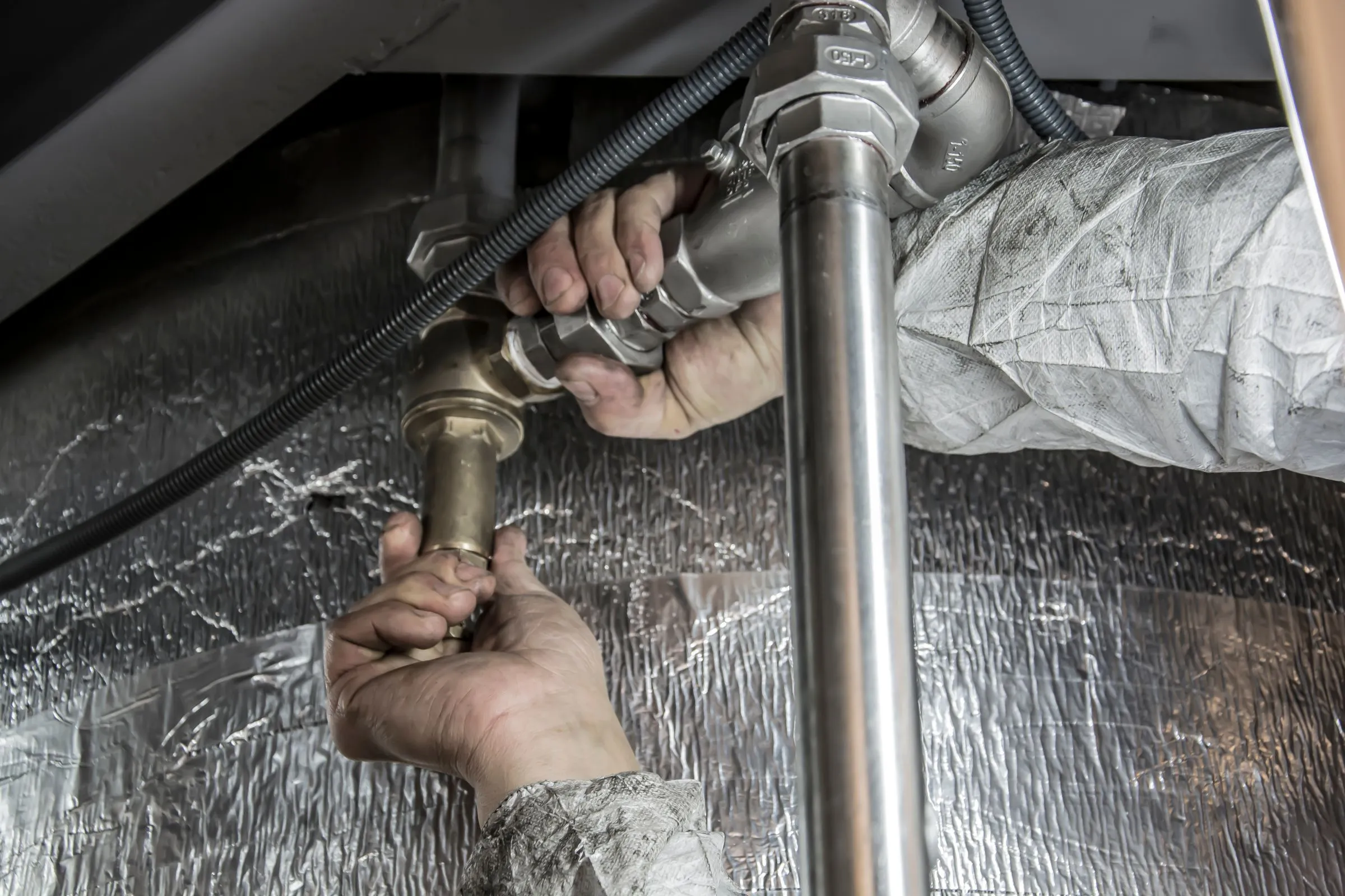 A plumber tightening a brass fitting on a new run of pipe under an insulated floor